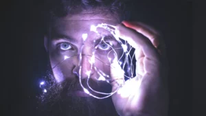 A bearded man holding a string of lights