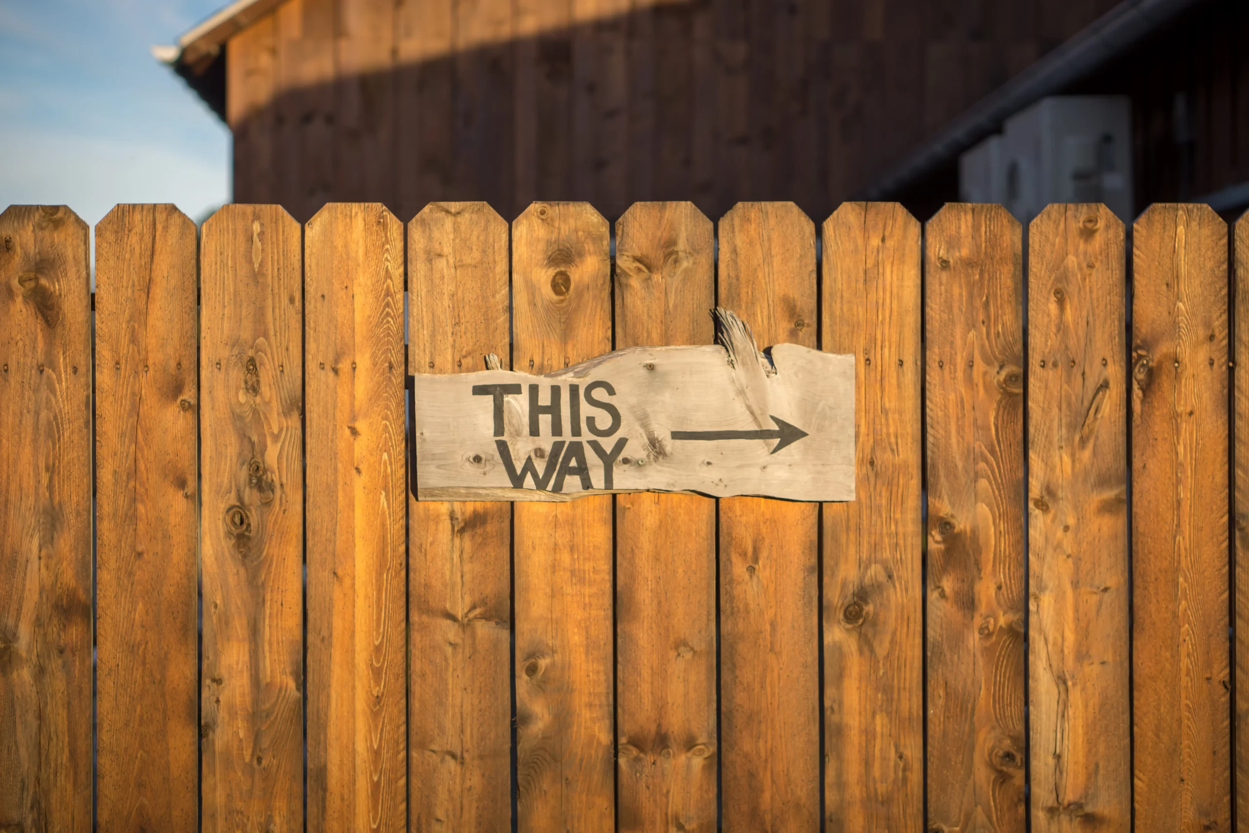 A wooden fence sign pointing the way, indicating a direction