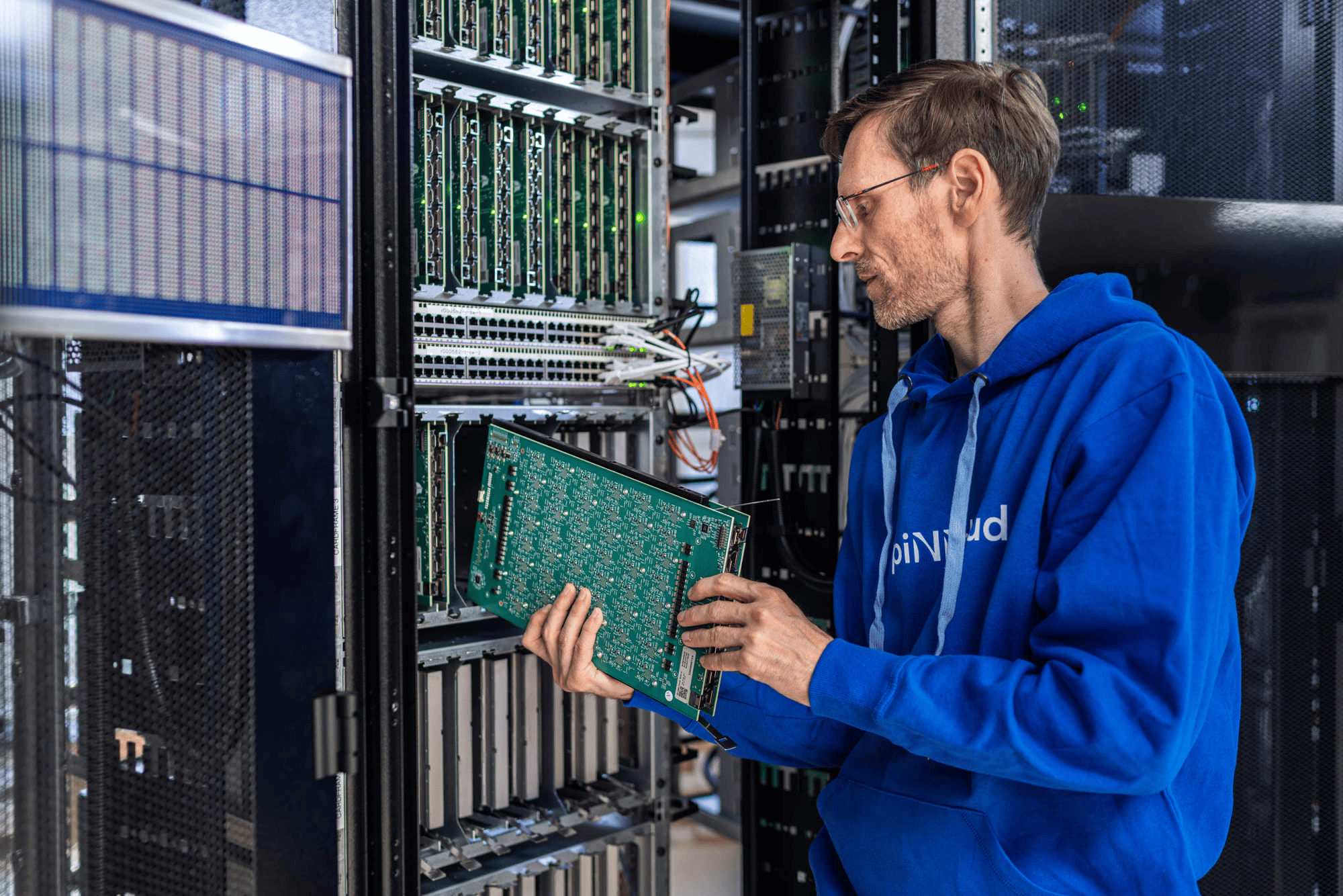 A man in a blue hoodie installs or removes a circuit board from a server rack in a data center
